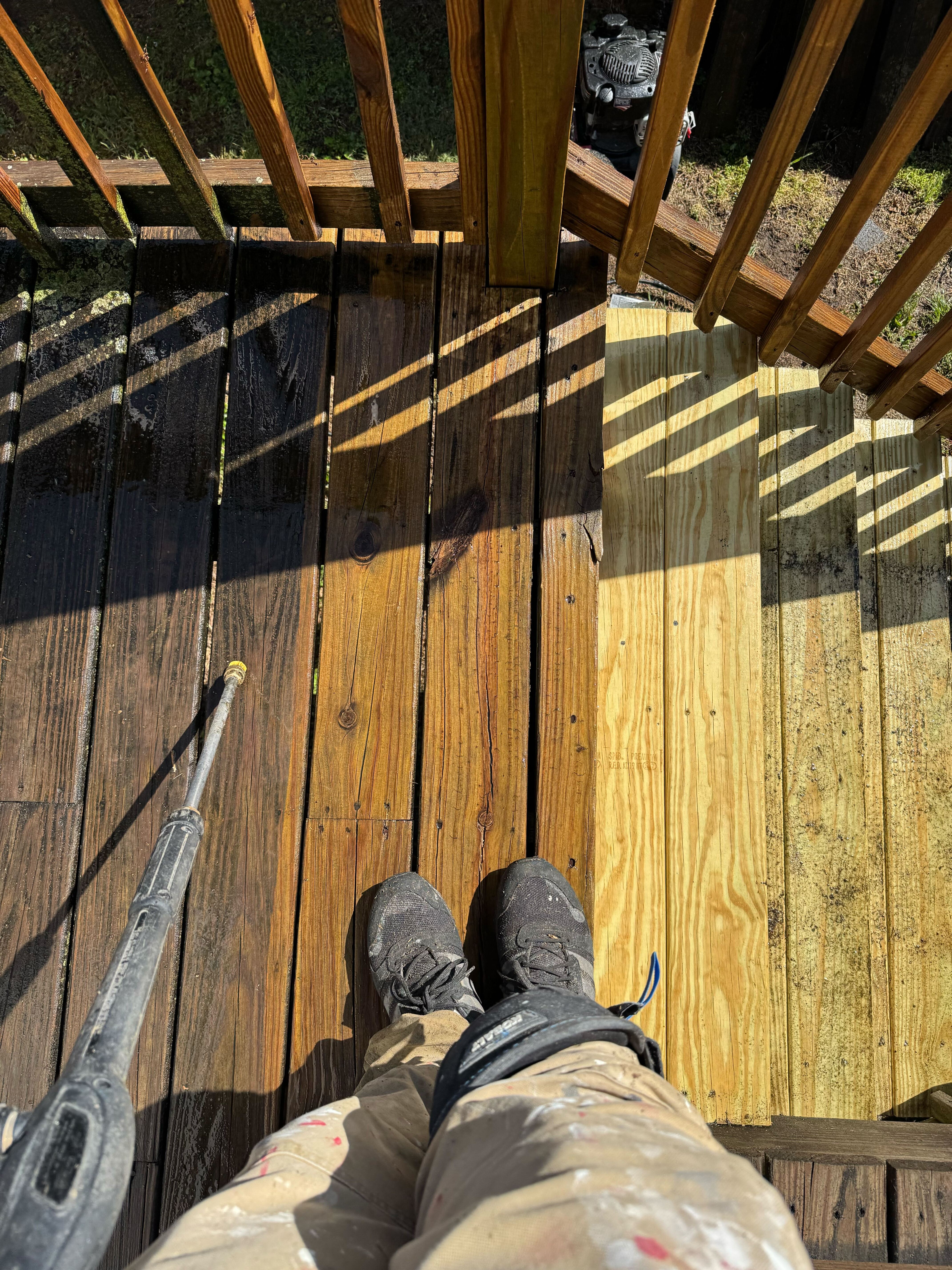 Crew member pressure washing wooden deck with pergola overhead